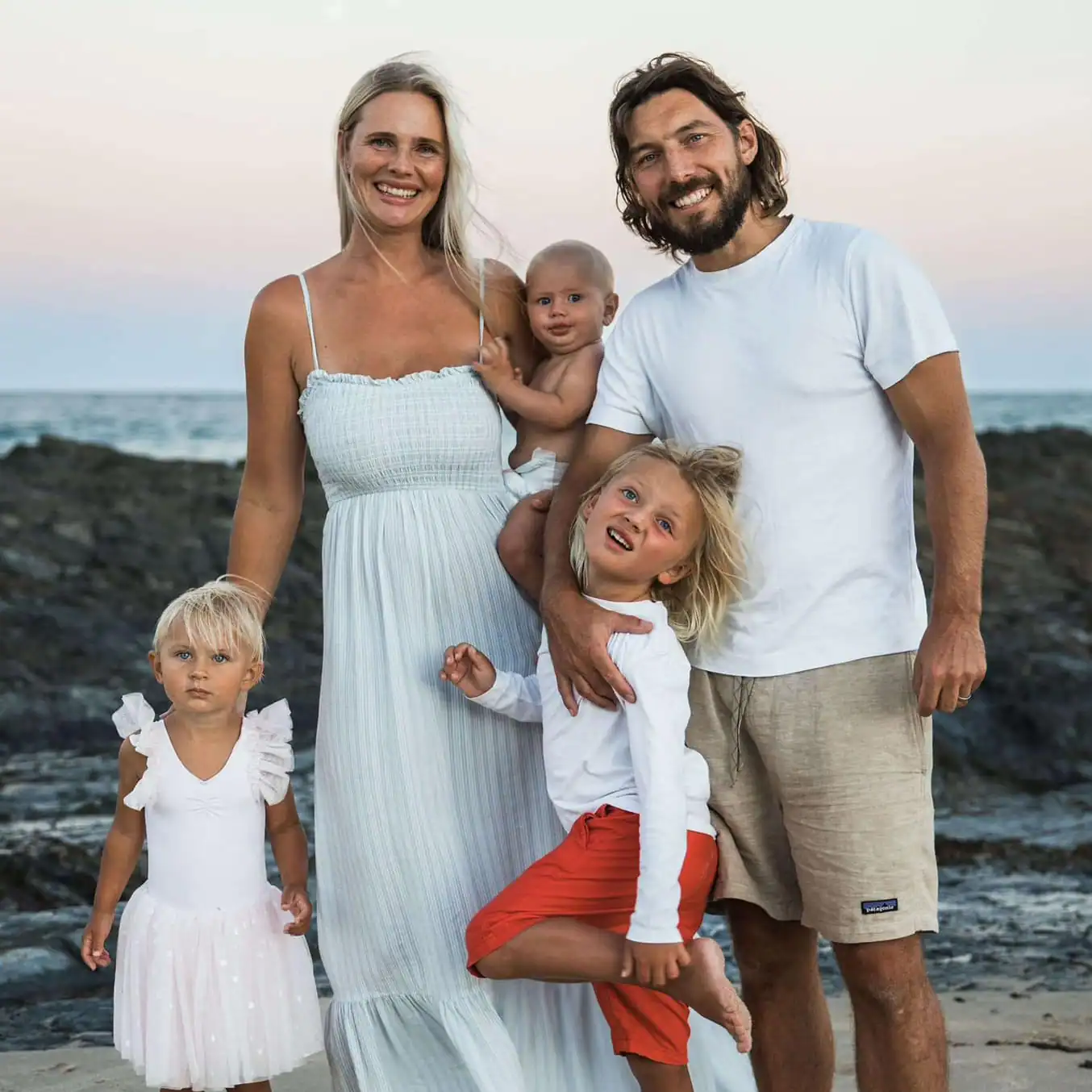 Familj med två vuxna och tre barn på stranden vid solnedgången.
